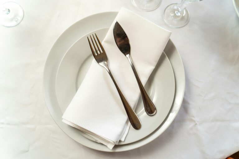 plate setting with fork, butter knife, and napkin on white table cloth