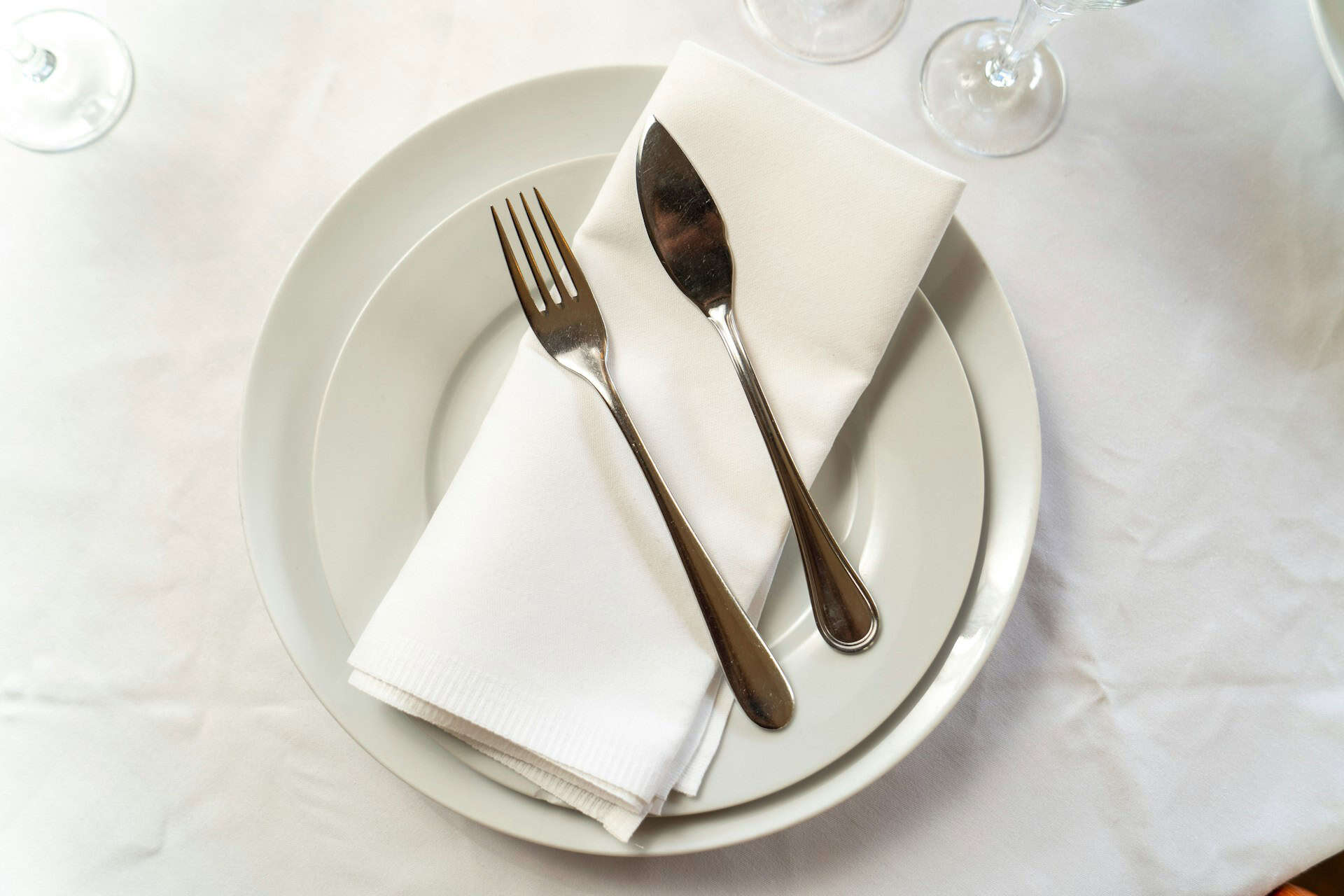 plate setting with fork, butter knife, and napkin on white table cloth